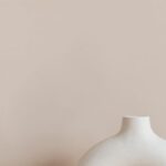 Co-Living Spaces - White ceramic vase in creative shape of ring placed on white marble stand against beige wall as home decoration element or art object