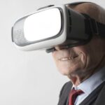 Reality Shows - Smiling elderly gentleman wearing classy suit experiencing virtual reality while using modern headset on white background