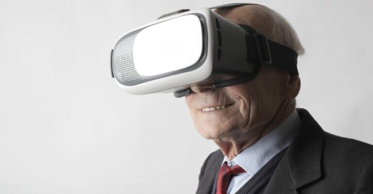 Reality Shows - Smiling elderly gentleman wearing classy suit experiencing virtual reality while using modern headset on white background