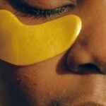 Morning Routines - Crop gentle African American female with closed eyes and clean face enjoying cosmetic procedure for smoothing and moisturizing skin under eyes and removing dark circles